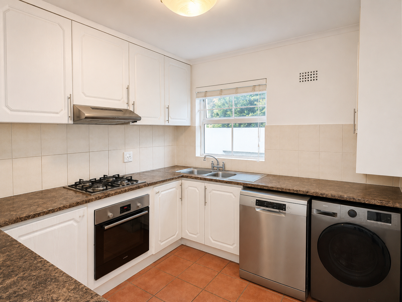 A functional kitchen featuring white cabinetry, laminate countertops, a gas hob, built-in oven, and tiled flooring with space for under-counter appliances.