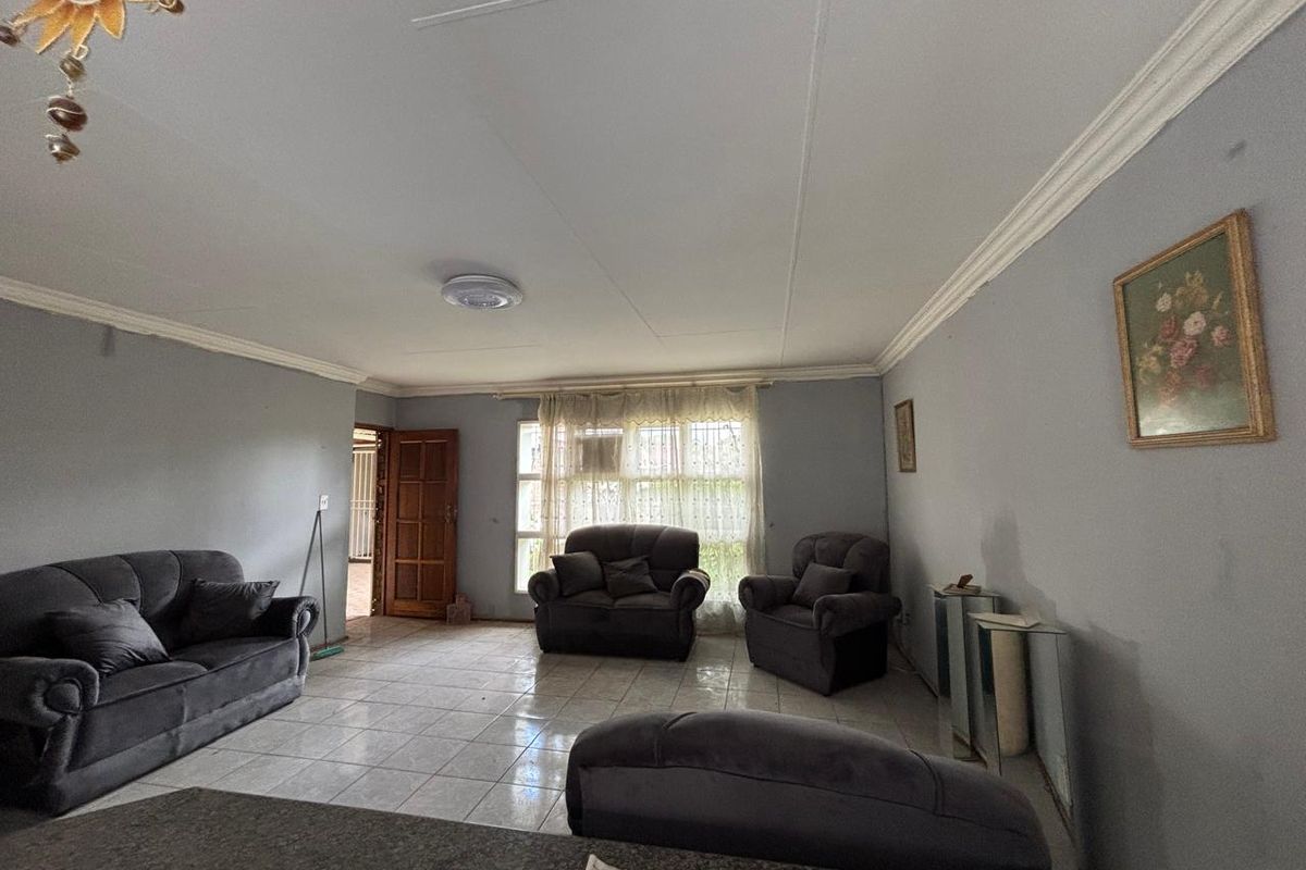 Spacious living room featuring tiled flooring, crown molding, and large windows allowing natural light, providing a comfortable and functional living space.