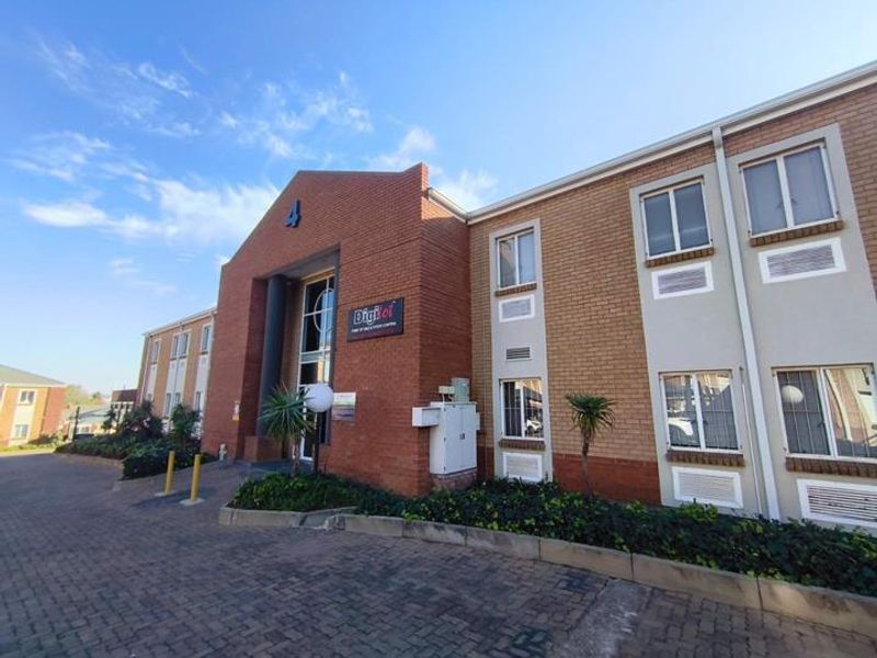 Front elevation of a multi-story brick office building featuring a paved driveway, landscaped garden beds, and integrated wall-mounted air conditioning units.