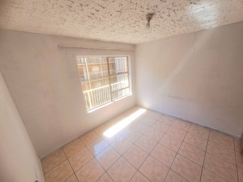 An empty bedroom featuring tiled flooring, a textured ceiling, and a window fitted with security bars.