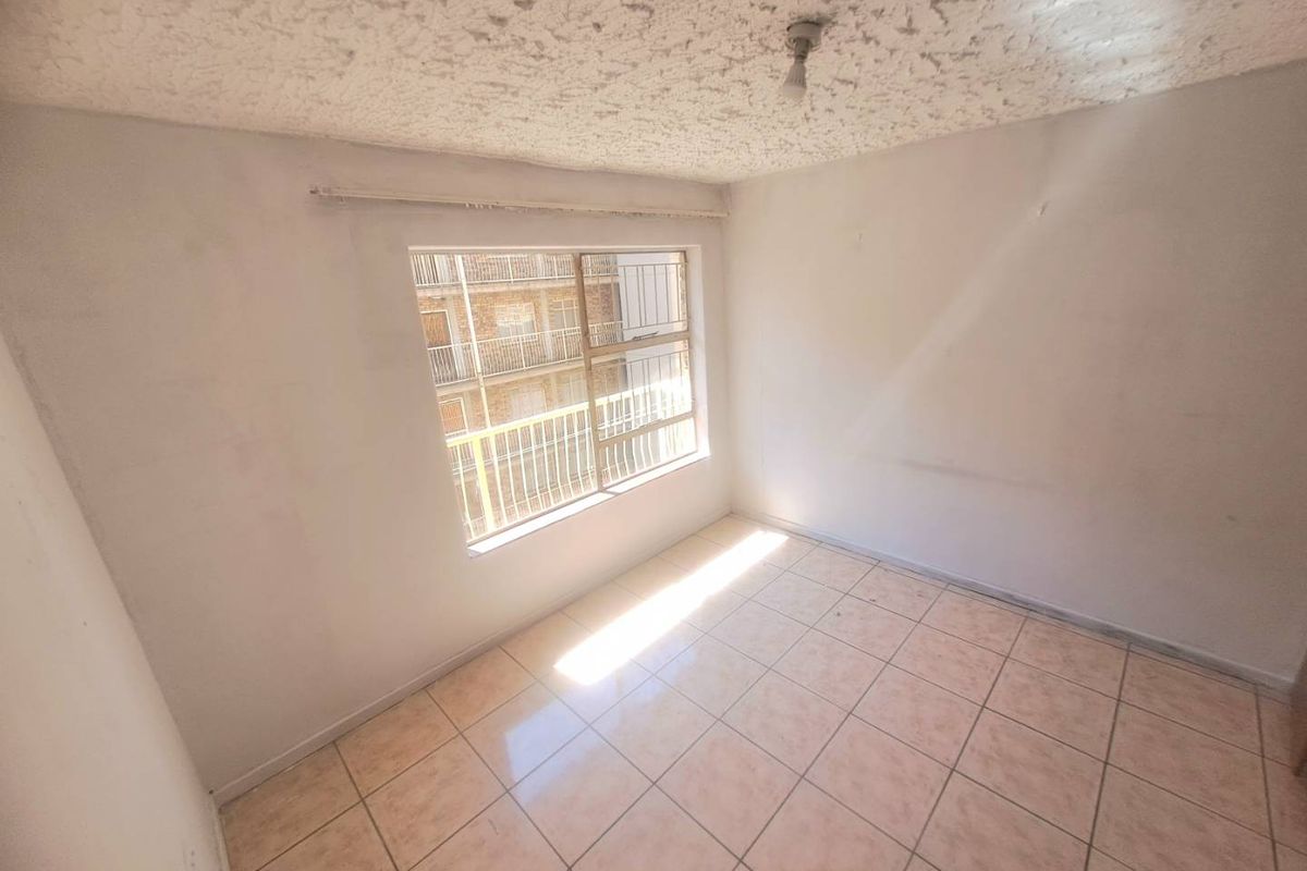 An empty bedroom featuring tiled flooring, a textured ceiling, and a window fitted with security bars.