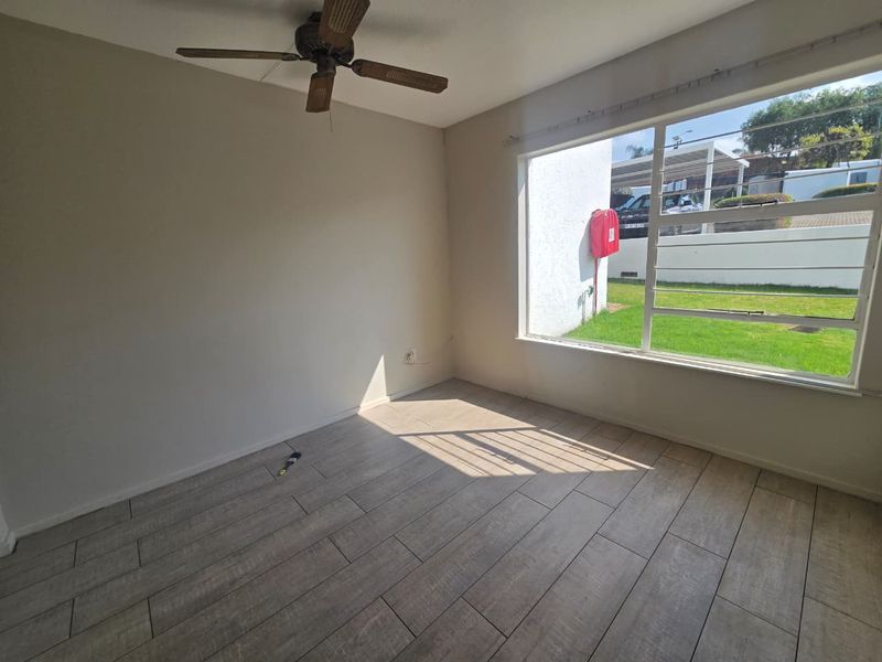 An empty living room featuring wood-look tiled flooring, a ceiling fan, and a large window providing natural light and views of the exterior.