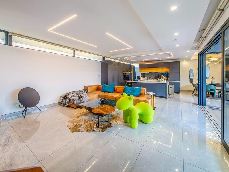 Modern open-plan living area featuring sleek tiled floors, recessed ceiling lighting, and a contemporary kitchen with a central island and integrated appliances.