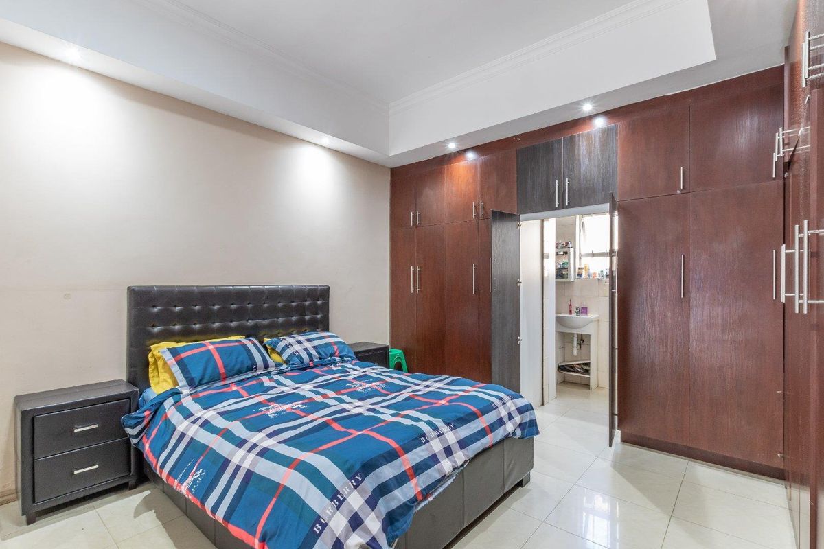Spacious bedroom featuring extensive built-in dark wood cabinetry, recessed ceiling lighting, and tiled flooring, with an integrated en-suite bathroom access.