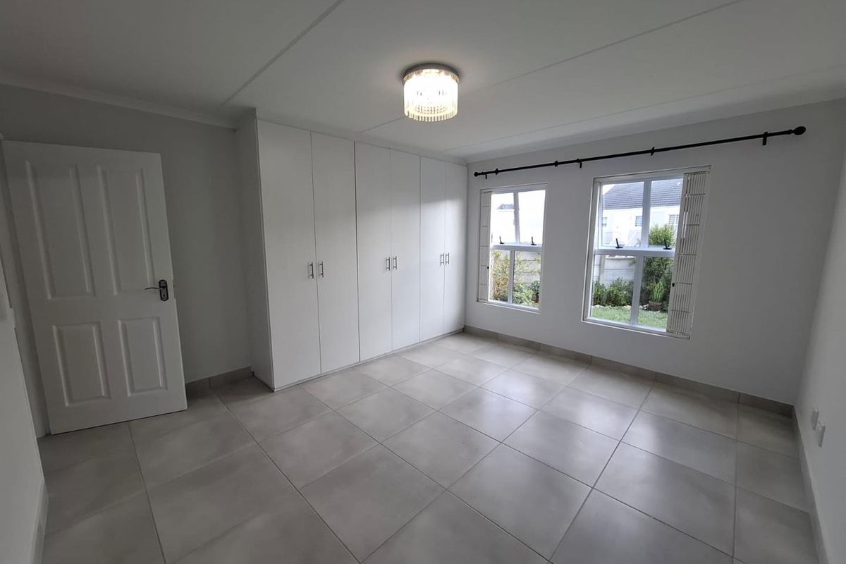 A bright, empty bedroom featuring neutral floor tiles, built-in white cabinetry, and large windows providing natural light.