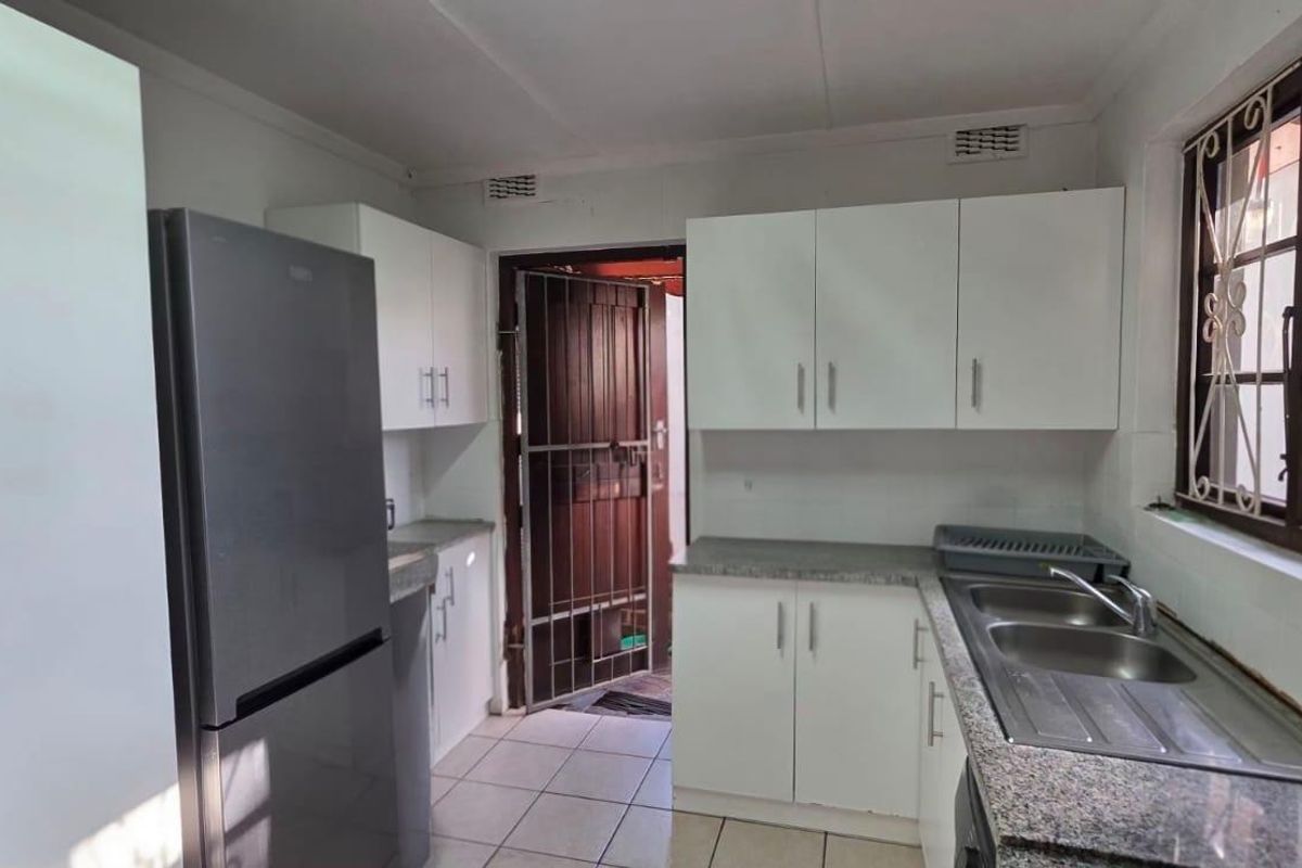 A functional kitchen featuring white cabinetry, granite countertops, a double bowl stainless steel sink, and tiled flooring with direct access to the exterior.