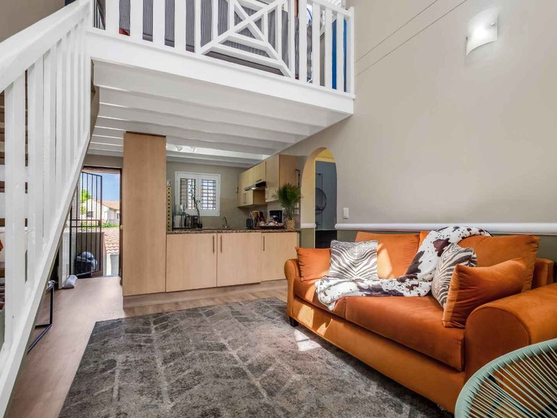Open-plan living area featuring a mezzanine level, staircase, and compact kitchen with built-in cabinetry and integrated fixtures.