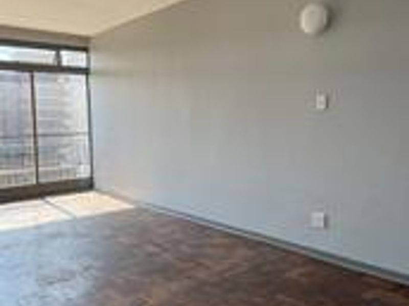 An empty living room featuring classic parquet flooring, a large sliding glass door providing natural light, and neutral wall finishes.