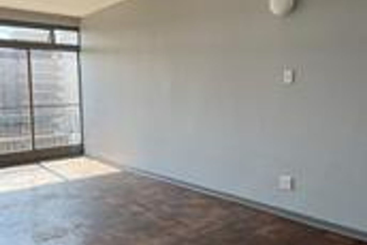 An empty living room featuring classic parquet flooring, a large sliding glass door providing natural light, and neutral wall finishes.
