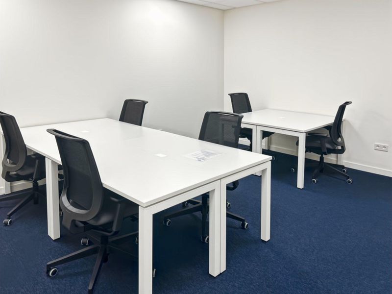A clean, functional office space featuring blue carpeting, white walls, and integrated electrical outlets, suitable for a professional work environment.