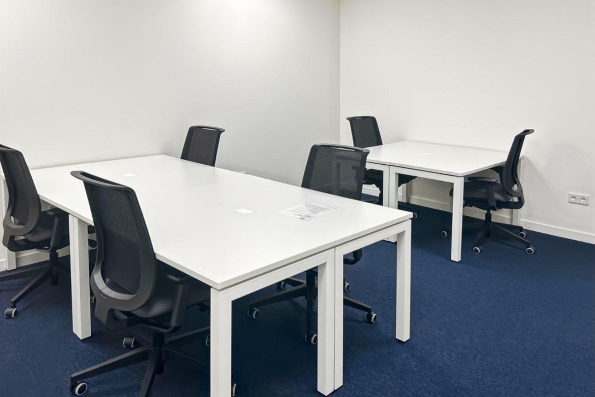 A clean, functional office space featuring blue carpeting, white walls, and integrated electrical outlets, suitable for a professional work environment.