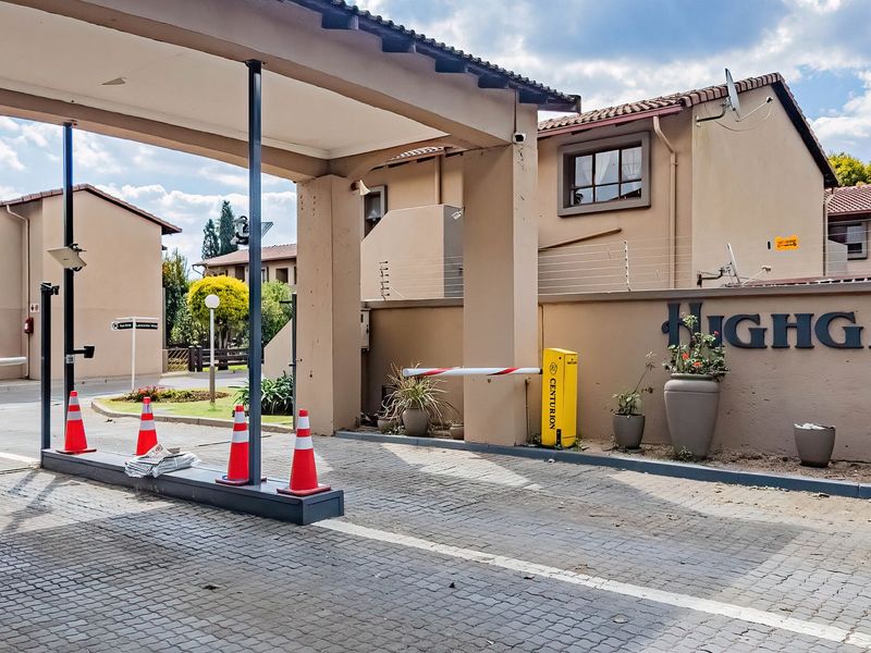 The entrance to Highgate complex featuring a secure boom gate, paved driveway, and perimeter electric fencing.