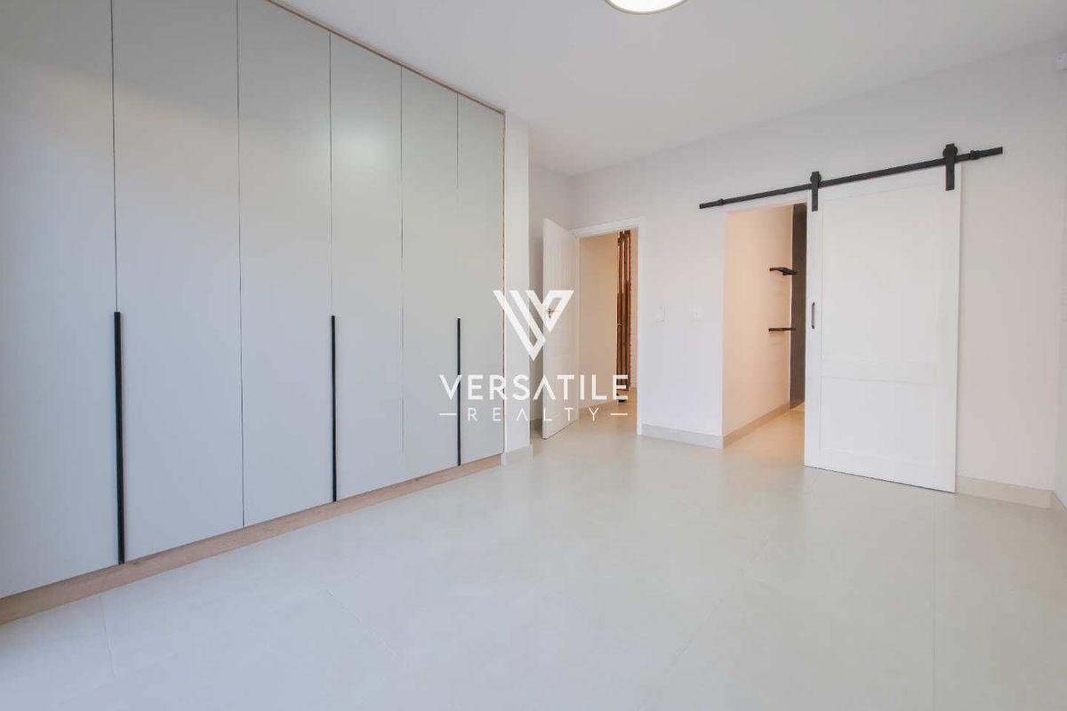 A bright, modern bedroom featuring extensive built-in cupboards, neutral tiled flooring, and a stylish sliding barn door leading to an adjoining space.