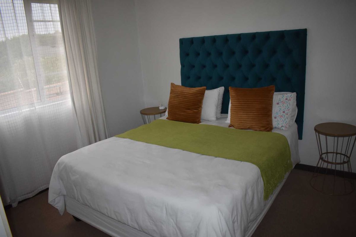 A well-lit bedroom featuring neutral carpeting and a large window with sheer curtains, providing a comfortable and functional sleeping space.