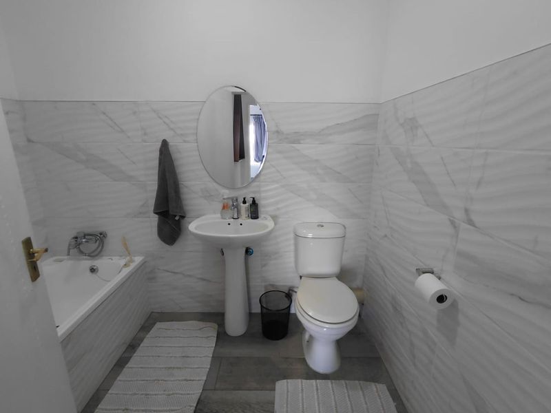 A clean, modern bathroom featuring marble-effect wall tiling, a pedestal washbasin, a toilet, and a bathtub.