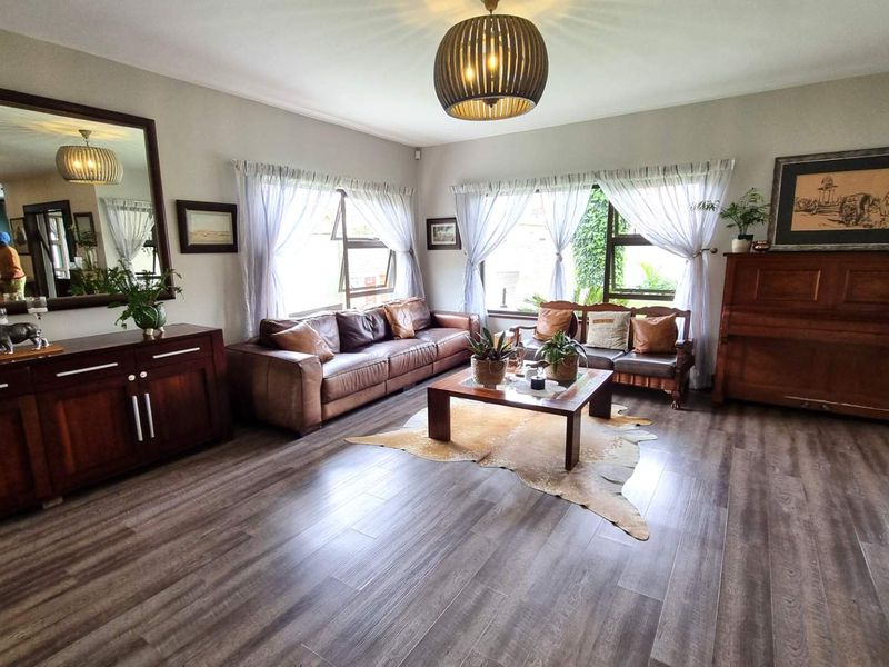 Spacious living room featuring modern laminate flooring, large windows with natural light, and a prominent wall mirror, creating a bright and inviting atmosphere.