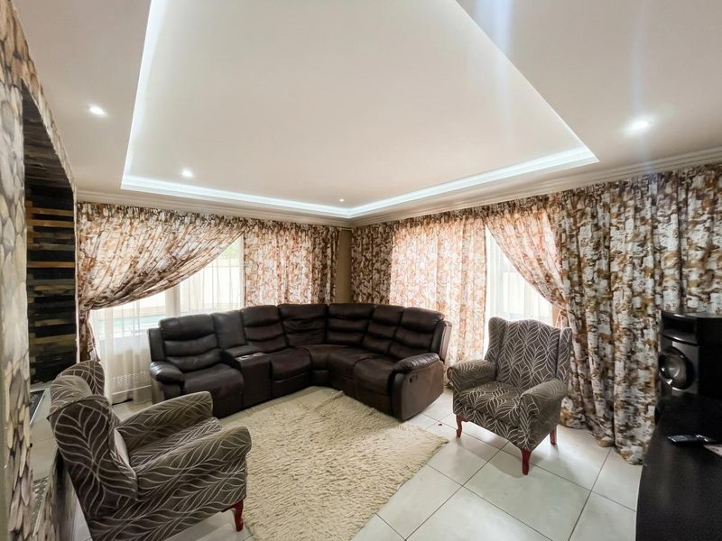 Spacious living room featuring a modern recessed ceiling with cove lighting, tiled flooring, and a decorative stone feature wall.