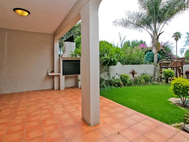 A covered patio featuring tiled flooring and a built-in braai, overlooking a private garden area.