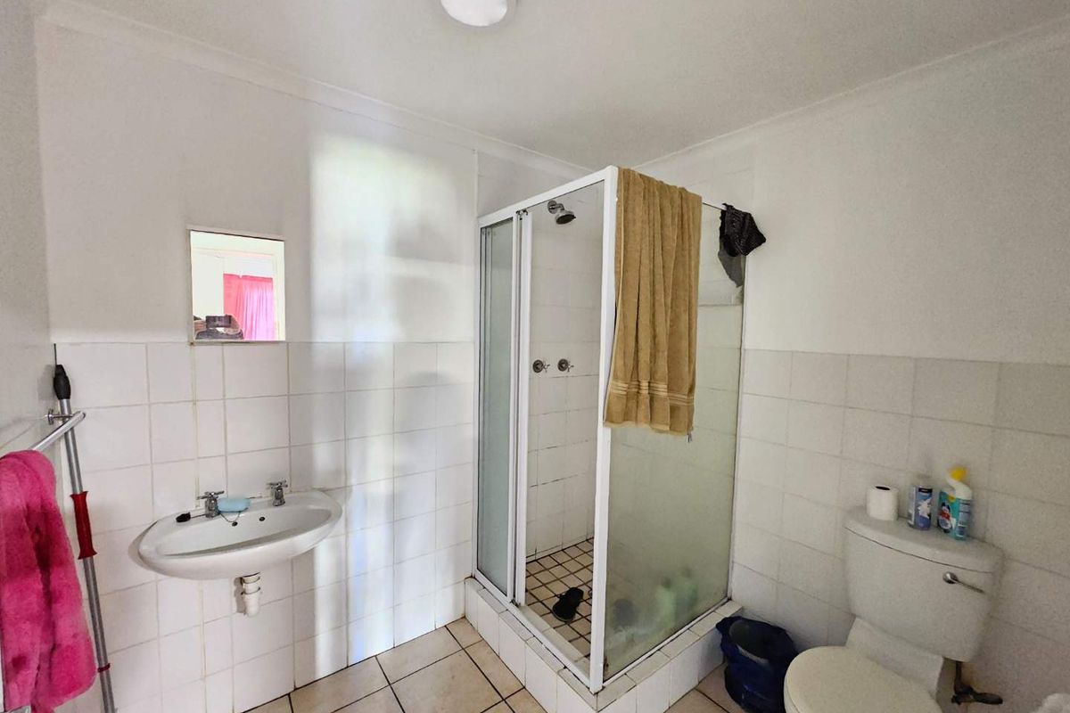 A functional bathroom featuring a wall-mounted basin, a corner shower enclosure with tiled base, and a standard toilet with white wall tiling.