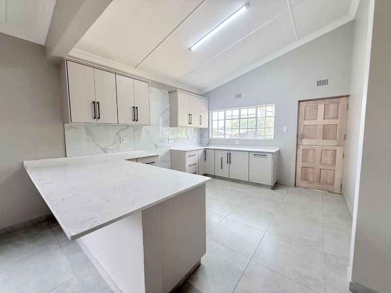 A modern, bright kitchen featuring clean white cabinetry, marble-look quartz countertops, tiled flooring, and a functional layout with ample workspace.