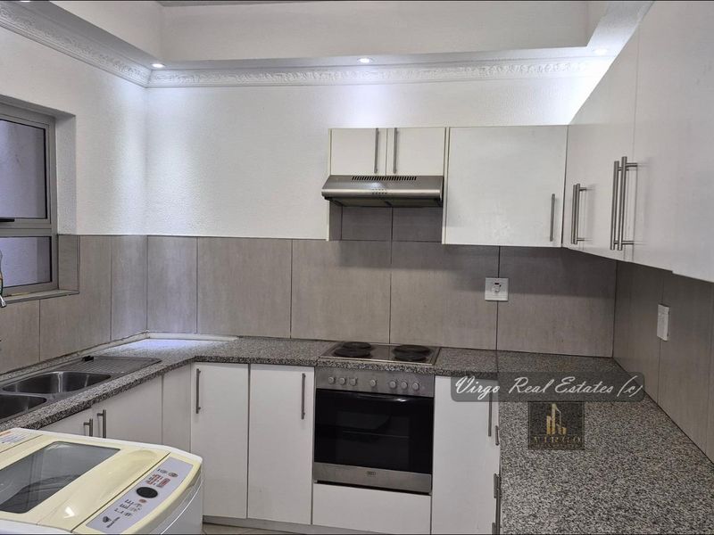 Modern kitchen featuring white cabinetry, granite countertops, built-in oven with hob, extractor fan, and a double bowl stainless steel sink with tiled splashback.