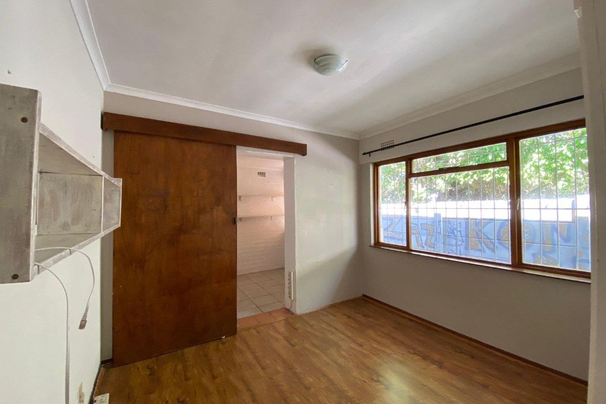 An empty bedroom featuring laminate flooring, a sliding wooden door, and security bars on the windows, offering a blank canvas for renovation.