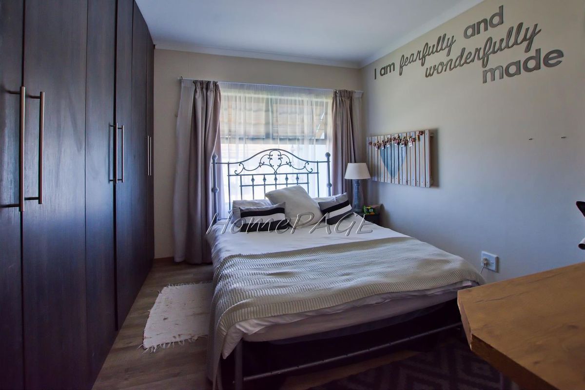 A bedroom featuring dark wood built-in cupboards, laminate flooring, and a window with curtain treatments.