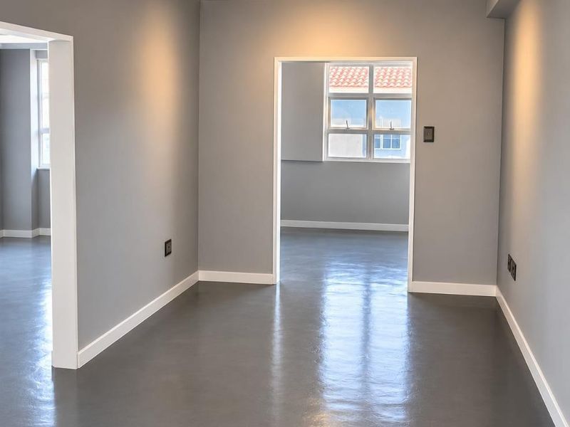 A bright, empty living area featuring polished concrete floors, modern track lighting, and elegant crown molding, offering a clean and contemporary blank canvas.
