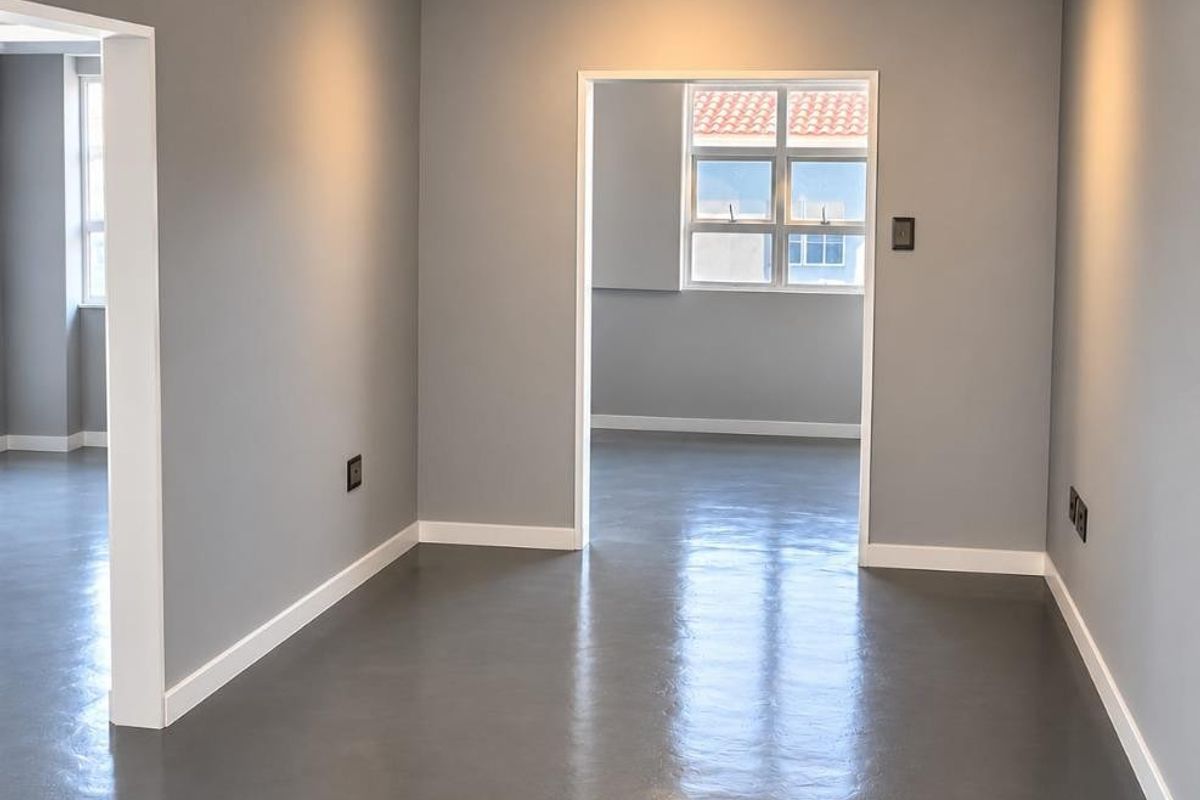 A bright, empty living area featuring polished concrete floors, modern track lighting, and elegant crown molding, offering a clean and contemporary blank canvas.