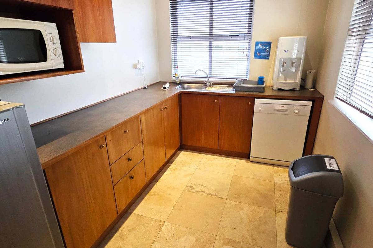 A functional office kitchenette featuring wood-veneer cabinetry, stone-look countertops, a stainless steel sink, and tiled flooring.