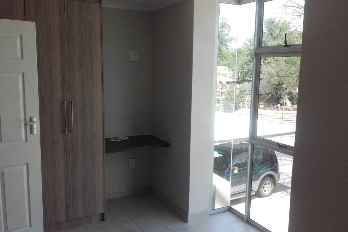 A bright bedroom featuring built-in wooden cabinetry, a wall-mounted desk, and large windows providing natural light and an exterior view.