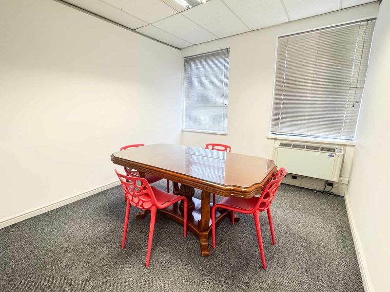 A functional office space featuring carpeted flooring, a suspended ceiling, and wall-mounted air conditioning, providing a clean and professional environment.