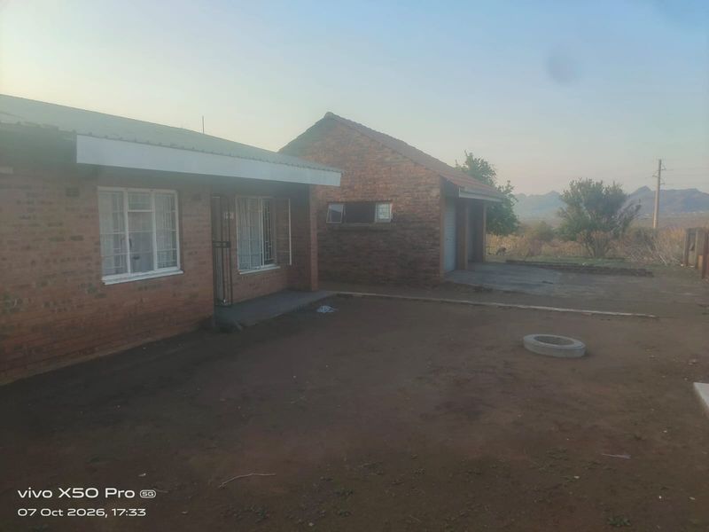 Rear view of a face brick house featuring a detached garage and an unpaved yard area.