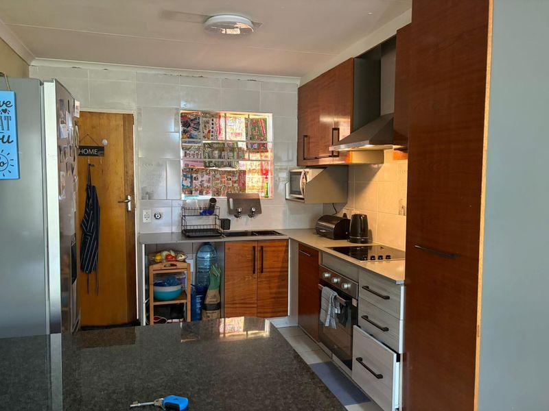 A functional kitchen featuring wood-finish cabinetry, granite countertops, built-in oven, and extractor fan, with a tiled backsplash and window view.