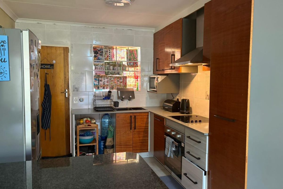 A functional kitchen featuring wood-finish cabinetry, granite countertops, built-in oven, and extractor fan, with a tiled backsplash and window view.