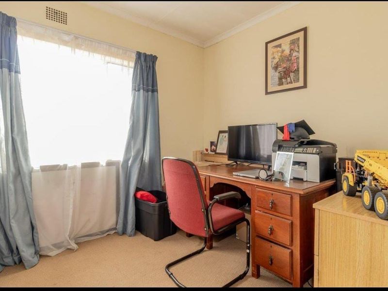 A functional home office space featuring neutral wall tones, carpeted flooring, and a large window allowing for natural light.