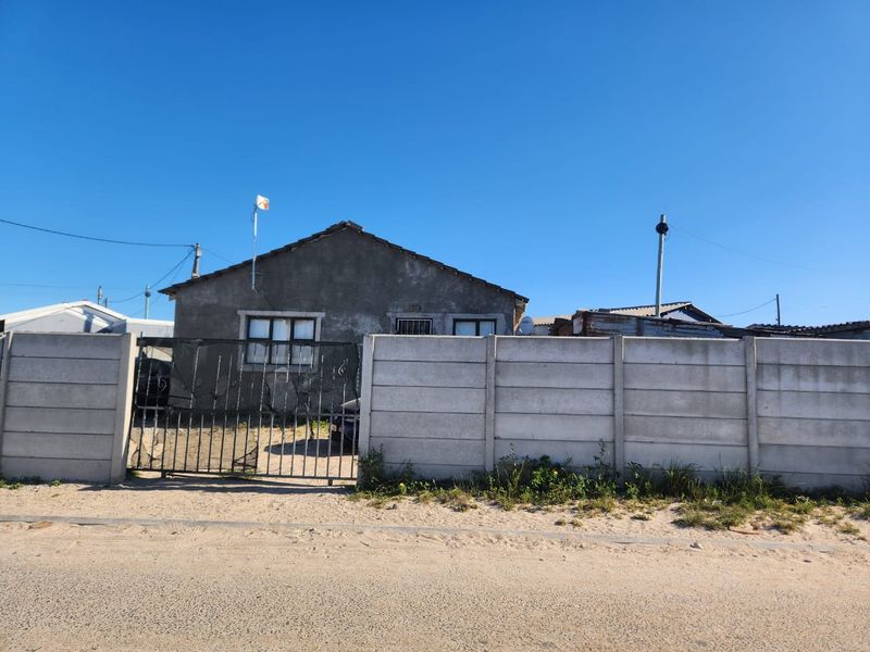 Front view of a single-story house featuring a precast concrete boundary wall, metal gate, and unpainted cement plaster exterior.
