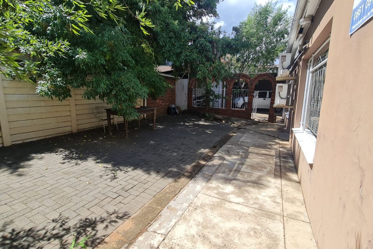 A paved rear courtyard area featuring brick archways, perimeter walling, and mature trees, providing a functional outdoor space for the office property.