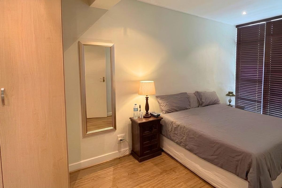A bedroom featuring light wood-look flooring, a built-in wardrobe, and window blinds, providing a functional and comfortable living space.
