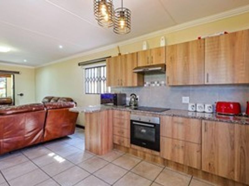 Open-plan kitchen and living area featuring wood-finish cabinetry, granite countertops, built-in oven, hob, and tiled flooring throughout.