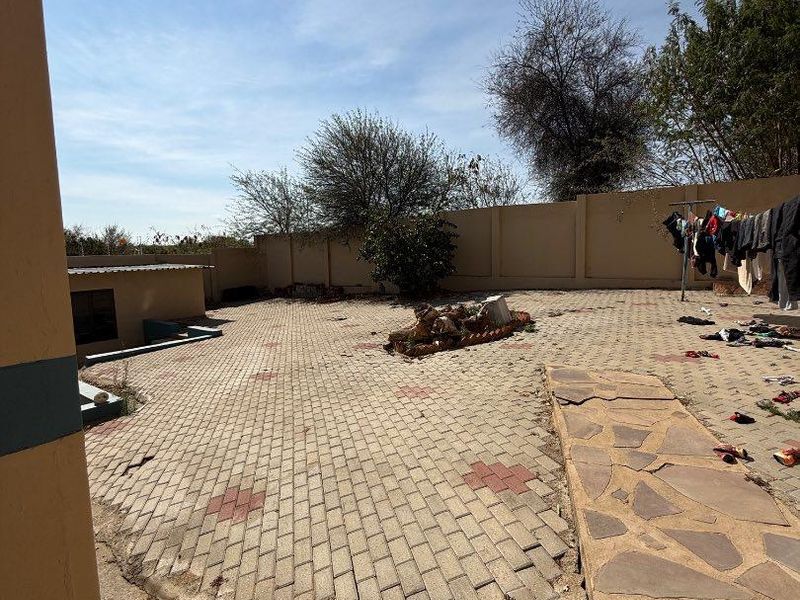 A spacious rear courtyard featuring paved surfaces and a perimeter wall, currently showing signs of wear and requiring maintenance to the paving and ground.