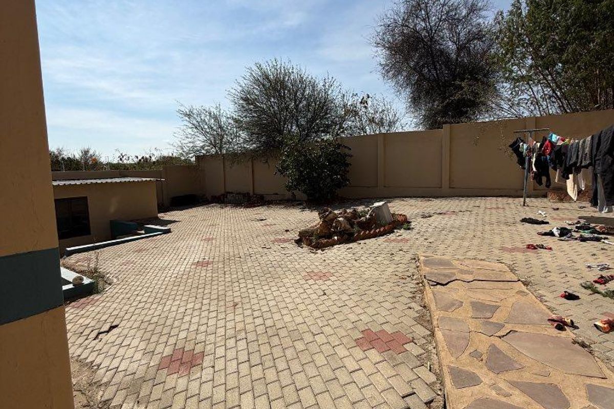 A spacious rear courtyard featuring paved surfaces and a perimeter wall, currently showing signs of wear and requiring maintenance to the paving and ground.
