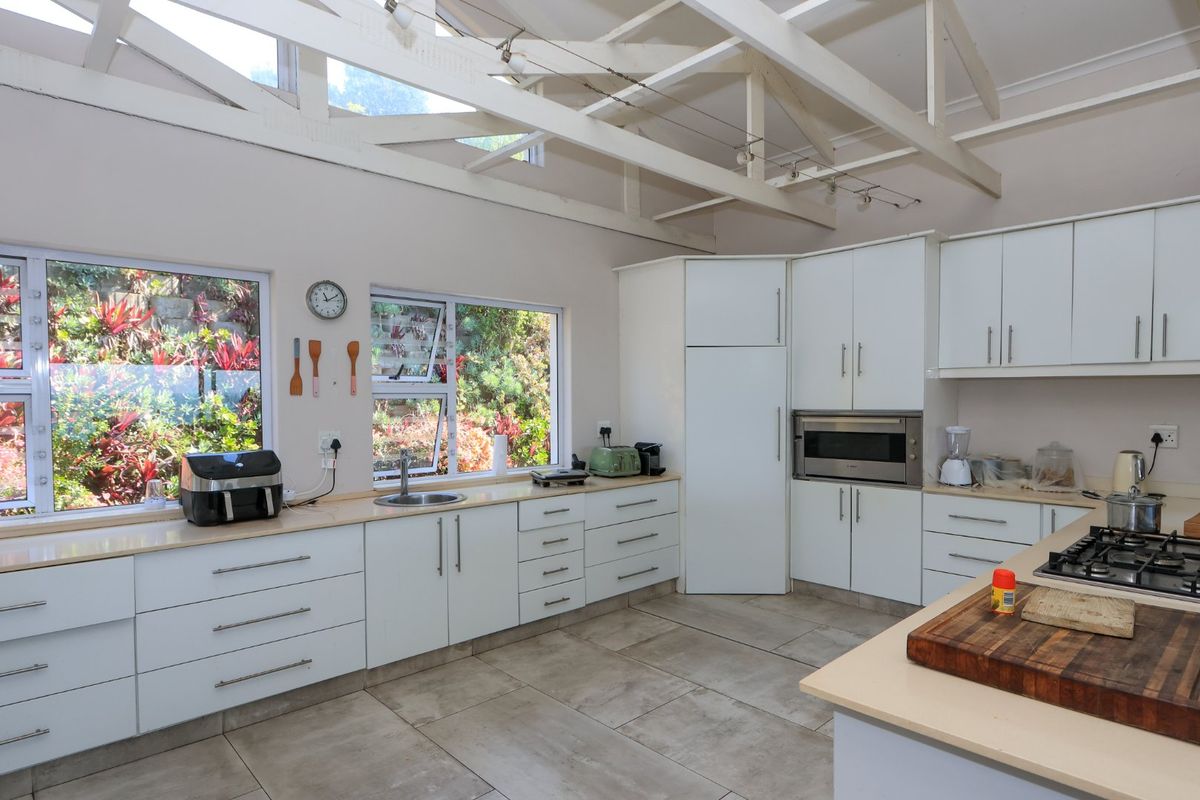 Spacious kitchen featuring white cabinetry, gas hob, built-in oven, tiled floors, and high ceilings with exposed trusses, offering ample natural light and workspace.