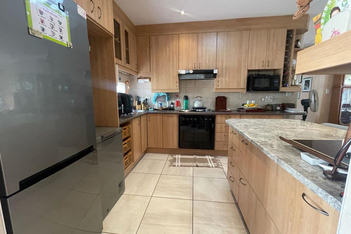 A functional kitchen featuring light wood cabinetry, stone-look countertops, a central island, and tiled flooring, providing ample storage and workspace.