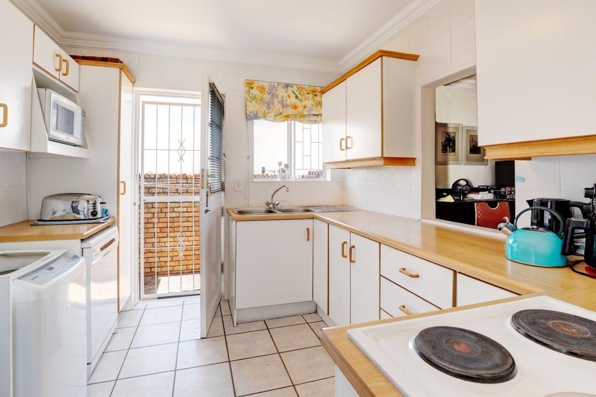 Functional kitchen featuring white cabinetry, wood-look laminate countertops, tiled flooring, and direct access to an exterior area.