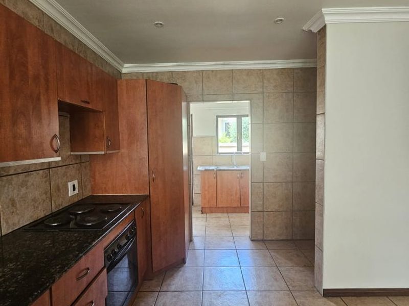 A functional kitchen featuring wood-finish cabinetry, granite countertops, integrated oven and hob, and tiled flooring, with an adjoining scullery area visible.