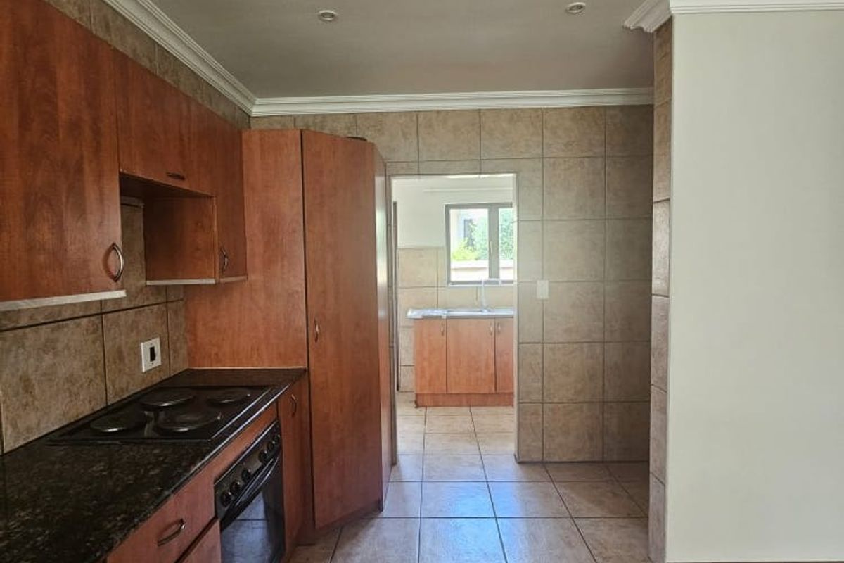 A functional kitchen featuring wood-finish cabinetry, granite countertops, integrated oven and hob, and tiled flooring, with an adjoining scullery area visible.