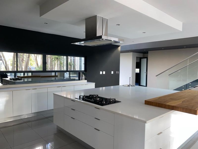 Modern open-plan kitchen featuring a large central island with gas cooktop, sleek white cabinetry, stone countertops, and integrated extractor fan.