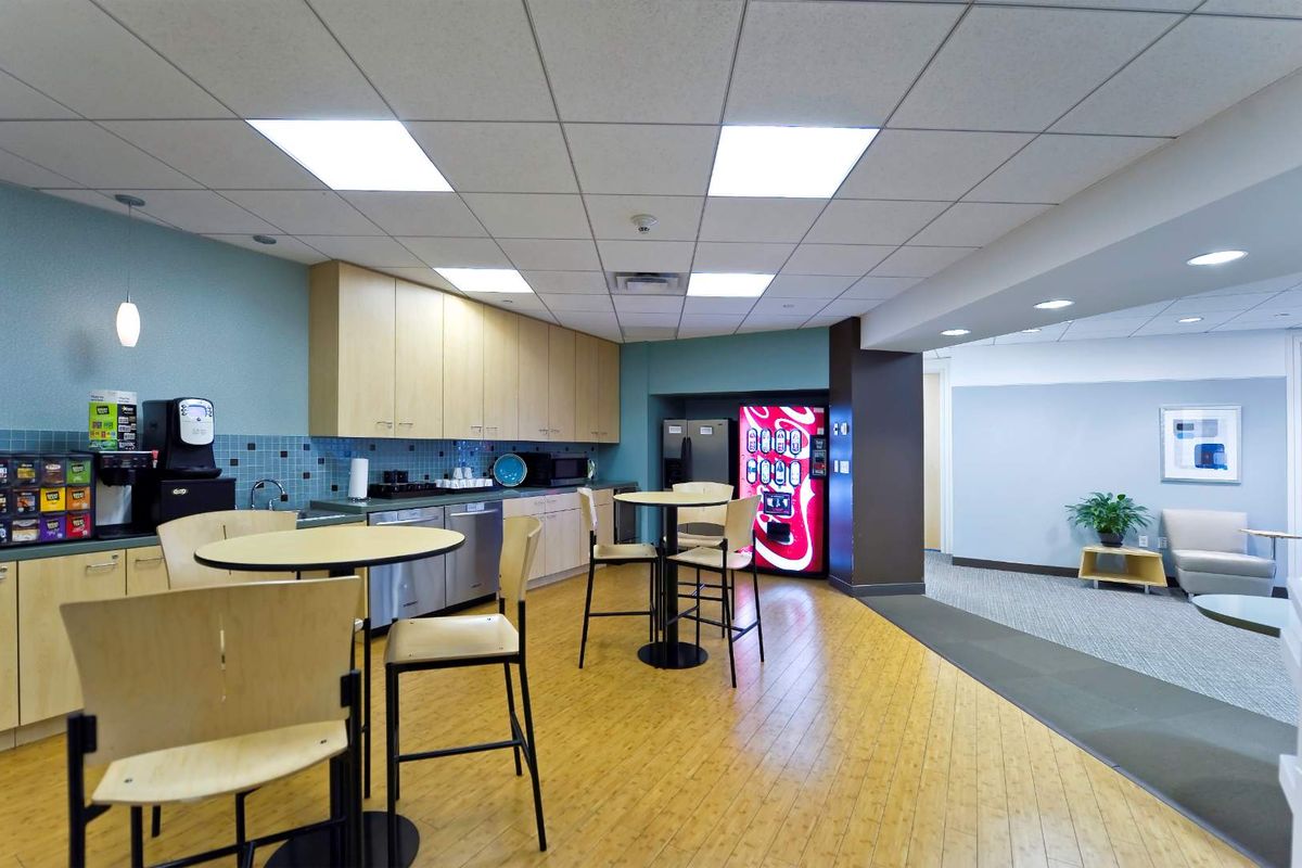 A functional office breakroom featuring a kitchenette with light wood cabinetry, tiled backsplash, integrated sink, and a dedicated vending machine area.