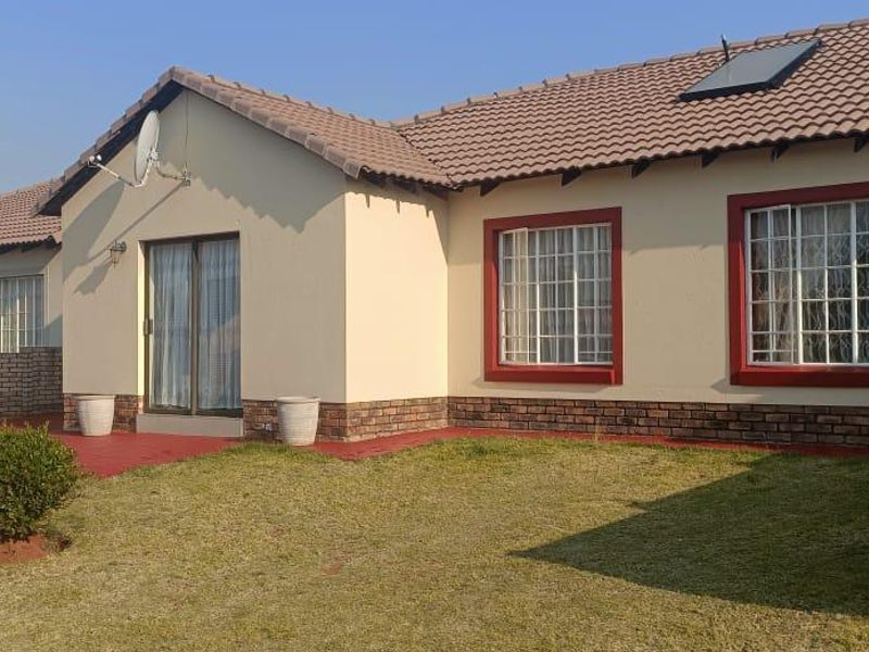 Rear view of a single-story house featuring a tiled roof, brick boundary walls, and a paved patio area accessible via sliding glass doors.